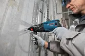 A person wearing safety equipment drills into a concrete wall along blue guide lines.