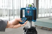 Person operates a laser leveling tool with a remote in a construction setting.