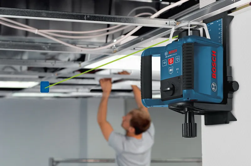 Laser leveling tool projecting a green line as a person installs a suspended ceiling.