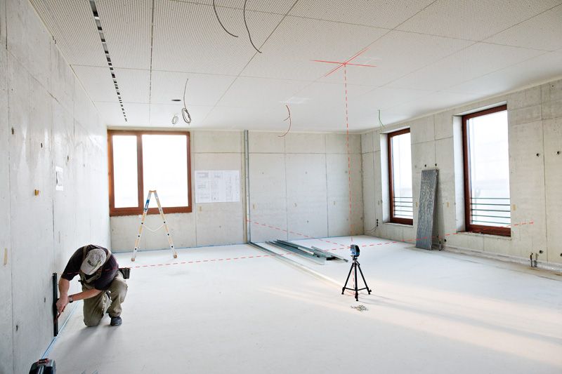 GCL 25 A person wearing safety equipment marks a wall using a laser leveling tool in a bright room.